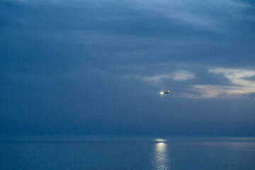 A plane coming in for landing at night, flying over the sea