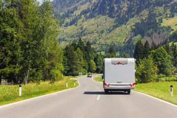 Scenic back view modern white family rv camper van vehicle drive Europe curvy road alpine pass mountain sunny summer day. Rving motorhome lifestyle travel adventure tourism trip Alps journey concept