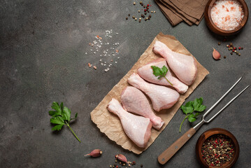 Raw chicken drumsticks on dark rustic background with spices flat lay