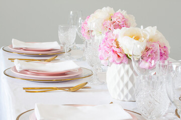 Elegant wedding table setting with pink peonies, gold cutlery, and crystal glassware, creating a romantic and sophisticated atmosphere.