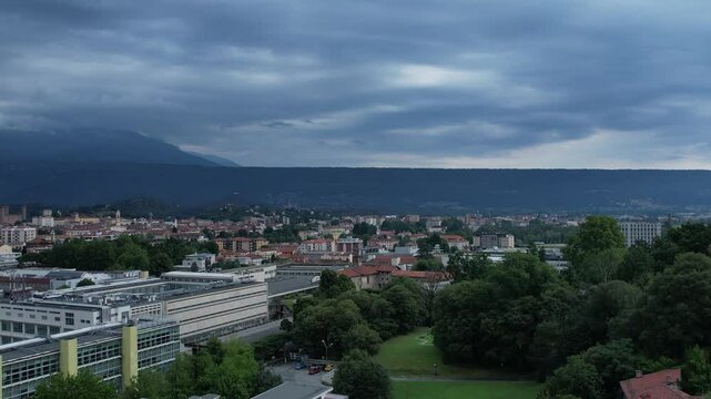 Modern glass-and-steel ICO IV building in Ivrea's Unesco-listed Olivetti district, framed by the Alps and Mount Mombarone in the background, drone shot, slow motion, sunny and cloudy sky