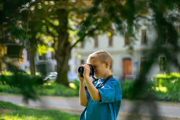 Cute boy in a blue t-shirt uses a digital camera and takes photos for his blog