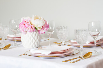 Elegant wedding table setting with pink peonies, gold cutlery, and crystal glassware, creating a romantic and sophisticated atmosphere.