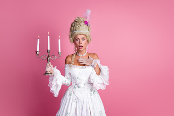 Sophisticated woman dressed in vintage European baroque costume holding candelabra against pink...