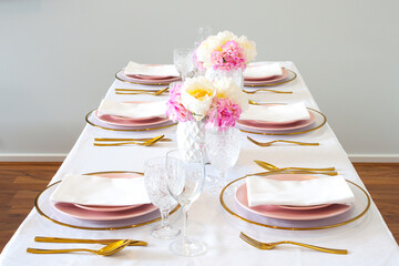 Elegant wedding table setting with pink peonies, gold cutlery, and crystal glassware, creating a romantic and sophisticated atmosphere.