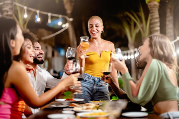 Group of friends enjoying a night out at an outdoor restaurant, laughing and toasting drinks under string lights in a lively, tropical setting.