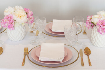 Elegant wedding table setting with pink peonies, gold cutlery, and crystal glassware, creating a romantic and sophisticated atmosphere.