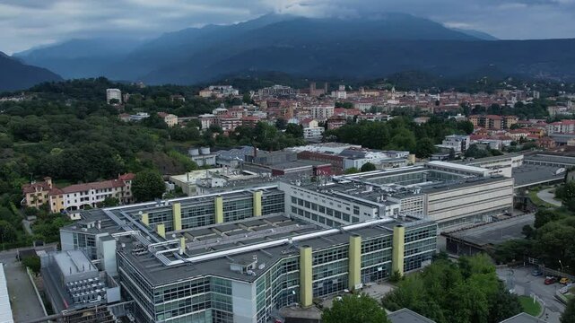 Modern glass-and-steel ICO IV building in Ivrea's Unesco-listed Olivetti district, framed by the Alps and Mount Mombarone in the background, drone shot, slow motion, sunny and cloudy sky