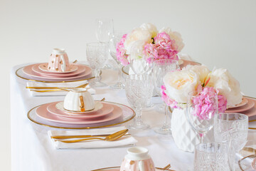 Elegant wedding table setting with pink peonies, gold cutlery, and crystal glassware, creating a romantic and sophisticated atmosphere.