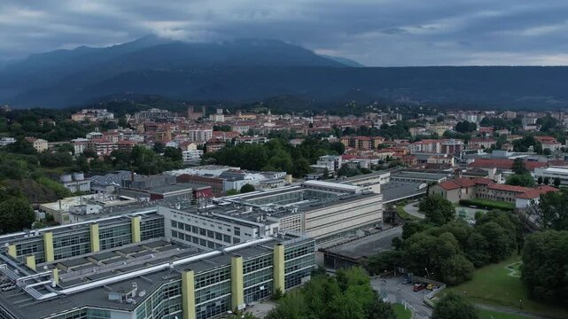 Modern glass-and-steel ICO IV building in Ivrea's Unesco-listed Olivetti district, framed by the Alps and Mount Mombarone in the background, drone shot, slow motion, sunny and cloudy sky