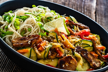 Asian food - pork tenderloin with stir fry vegetables and ramen noodles on wooden table