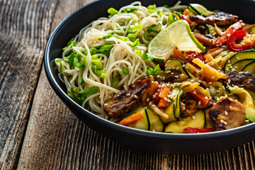 Asian food - pork tenderloin with stir fry vegetables and ramen noodles on wooden table