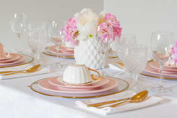 Elegant wedding table setting with pink peonies, gold cutlery, and crystal glassware, creating a romantic and sophisticated atmosphere.