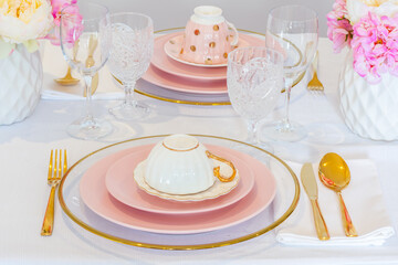 Elegant wedding table setting with pink peonies, gold cutlery, and crystal glassware, creating a romantic and sophisticated atmosphere.