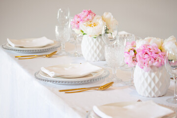 Elegant wedding table setting with pink peonies, gold cutlery, and crystal glassware, creating a romantic and sophisticated atmosphere.