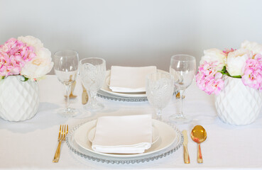 Elegant wedding table setting with pink peonies, gold cutlery, and crystal glassware, creating a romantic and sophisticated atmosphere.