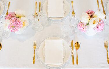 Elegant wedding table setting with pink peonies, gold cutlery, and crystal glassware, creating a romantic and sophisticated atmosphere.
