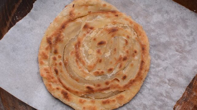 Overhead view of flaky paratha in a wooden bowl, top view of flaky flatbread, process of making paratha