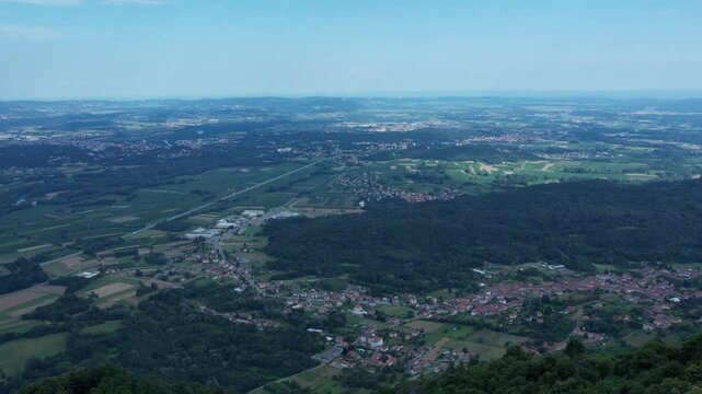 Drone panorama of the Ivrea Morainic Amphitheatre seen from Brosso, Val Chiusella, Italy, showing lush green plains, woods, and scattered villages under clear sky, high drone shot, slow motion