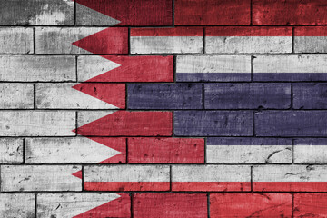 colourful painted big national flag of thailand and flag of bahrain on a massive old brick wall background. concept
