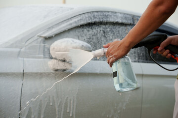 Man washing car with soap and water, creating bubbles and foam; outdoor car wash service focused on...