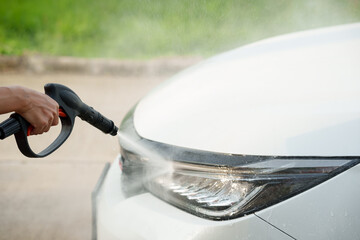 Man washing car with soap and water, creating bubbles and foam; outdoor car wash service focused on...