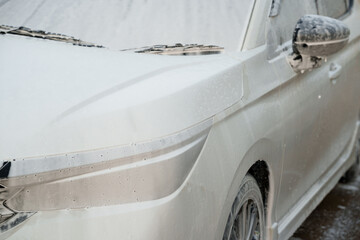 Man washing car with soap and water, creating bubbles and foam; outdoor car wash service focused on...