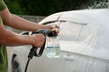 Man washing car with soap and water, creating bubbles and foam; outdoor car wash service focused on cleanliness, shine, and care.
