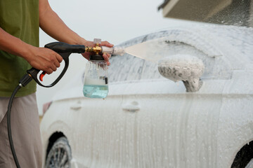 Man washing car with soap and water, creating bubbles and foam; outdoor car wash service focused on...
