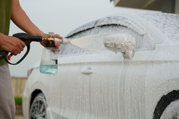 Man washing car with soap and water, creating bubbles and foam; outdoor car wash service focused on...