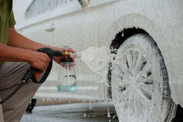 Man washing car with soap and water, creating bubbles and foam; outdoor car wash service focused on...