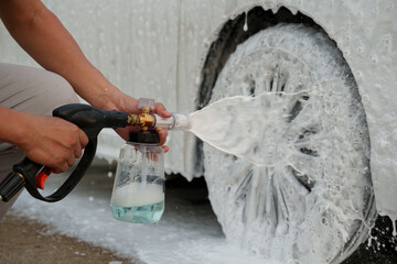 Man washing car with soap and water, creating bubbles and foam; outdoor car wash service focused on...