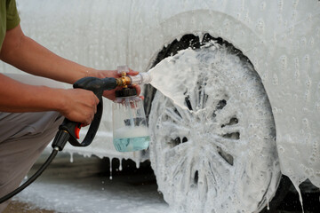 Man washing car with soap and water, creating bubbles and foam; outdoor car wash service focused on...
