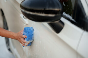 Man washing car with soap and water, creating bubbles and foam; outdoor car wash service focused on...