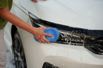 Man washing car with soap and water, creating bubbles and foam; outdoor car wash service focused on...