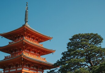 Orange pagoda near a tree in Kyoto, Japan, set against a clear blue sky, tourism