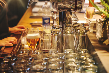 Close-up of a bar counter with a freshly poured draft beer, clean glasses, and bartender’s hands in a warm, ambient setting. Ideal for hospitality or nightlife themes.