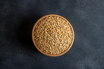 Wooden bowl in wheat grains on gray background,top view