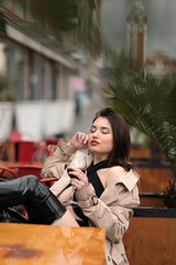 Beautiful sexy girl in a top and coat in a cafe with a glass of wine. put her feet up on the table