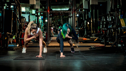 Focused women performing shoulder taps in plank position during high-intensity core workout,...