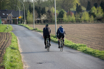 Naklejka premium Road cyclists ride through a scenic countryside path between summer fields in rural Europe, showcasing outdoor sports, nature, and provincial landscapes.