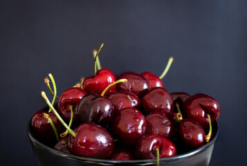 Lot of cherries in a bowl against a black background.