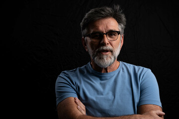 Mature man with beard emerging from darkness on black chiaroscuro background, positive expression