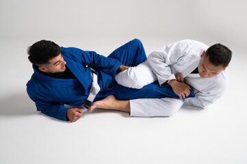 Two jiu jitsu athletes performing a leg lock on white background