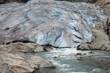 Close-up photo of the blue part of the Nigardsbreen glacier and the fast flowing water flowing from beneath it, in the Jostedalsbreen National Park in Norway