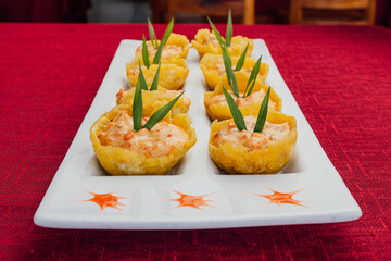 Patacones rellenos con salsa de camarón, sobre plato blanco.