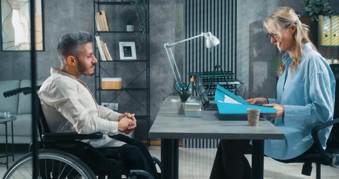 A man with a disability attends a job interview, where he presents his CV and speaks with the female leadership in the office.