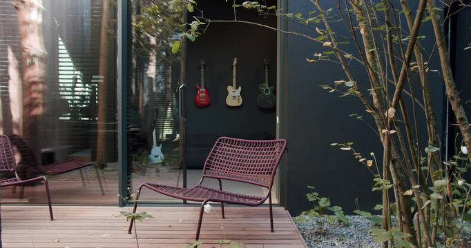Chairs on modern house terrace. Pan right view of comfortable chairs placed on terrace near glass wall and door of home studio outside contemporary house. Stylish Outdoor Patio With Elegant Seating