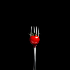 A Single Red Cherry Tomato Balanced on a Fork Against a Black Background: A Minimalist Food Photography Image