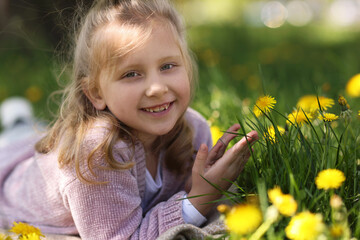 Cute little girl among beautiful dandelions outdoors on sunny day